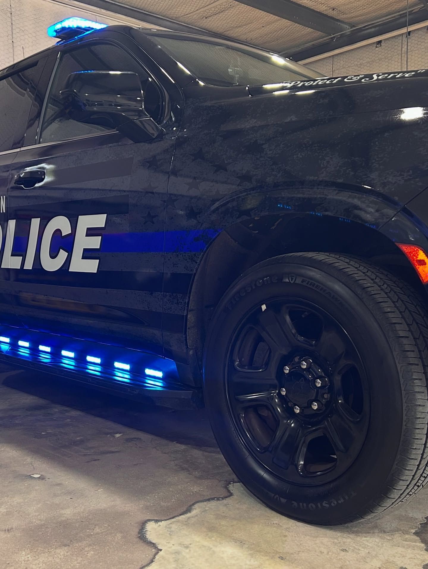 Black police SUV with blue emergency lights, parked indoors. 