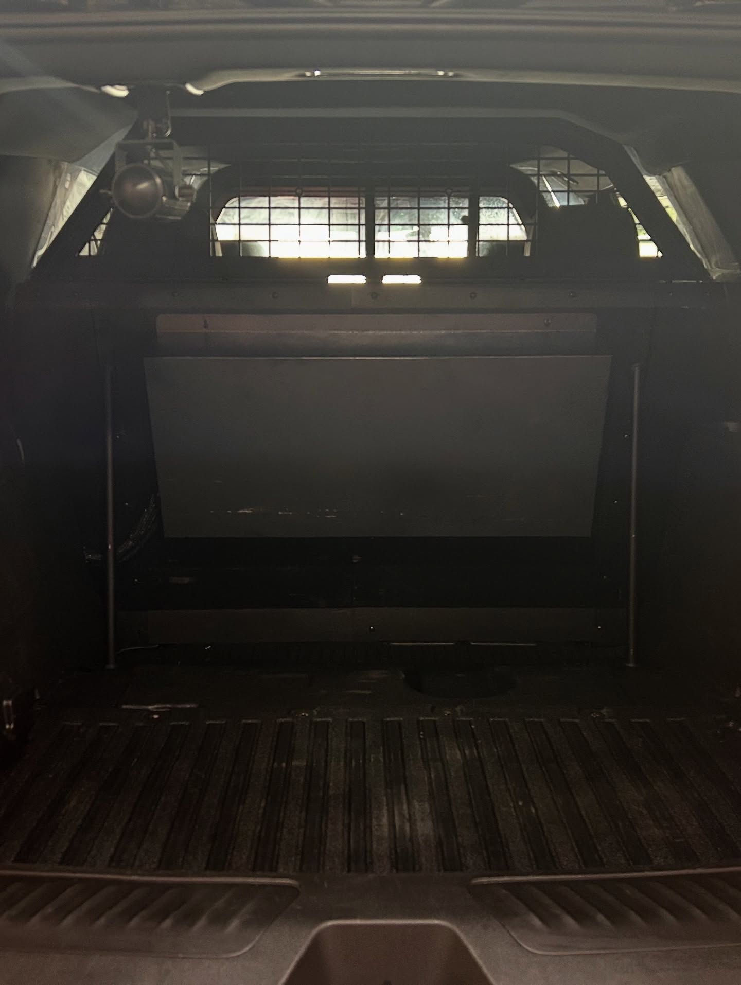 Dark interior view of a truck bed with a metal grate and a large, flat, dark-colored surface.