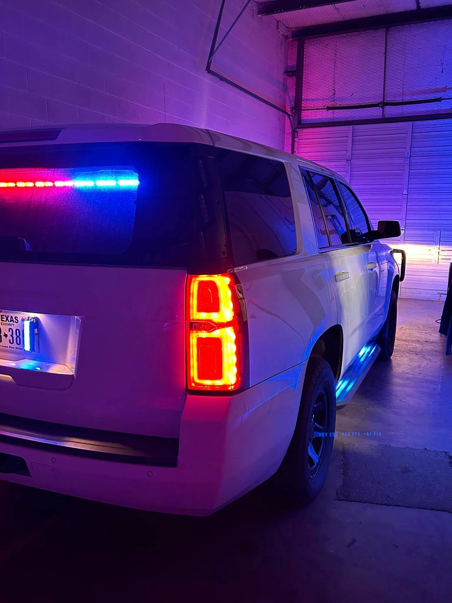 White SUV with red and blue emergency lights in a garage, illuminated with purple and blue lights.