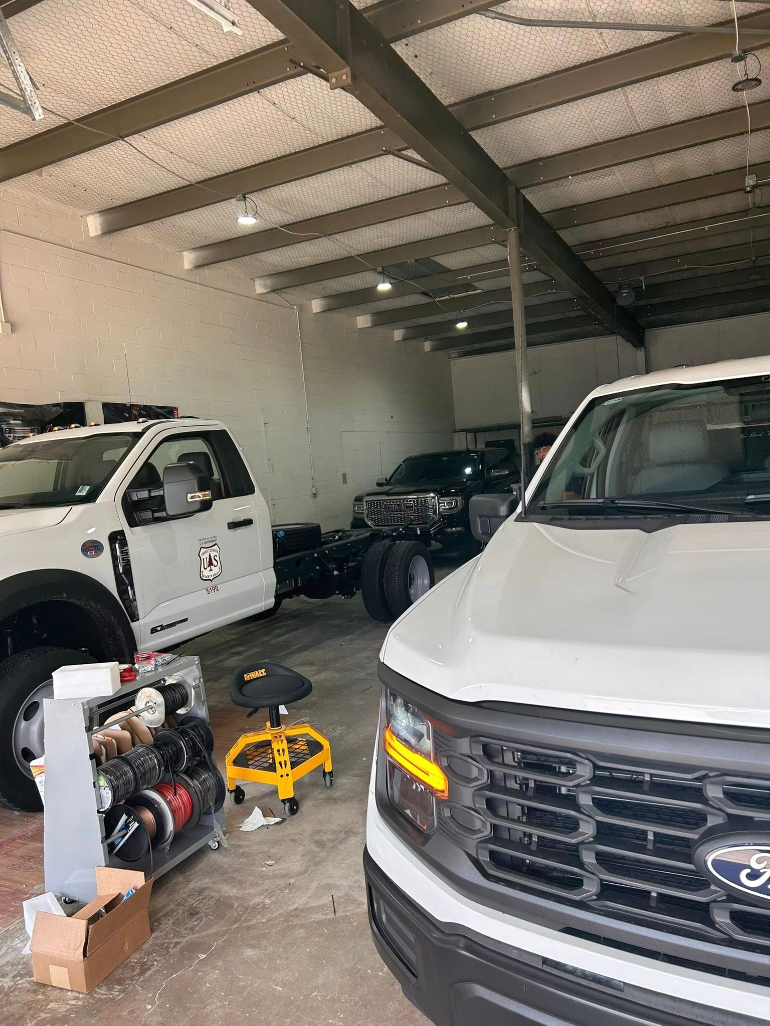 White Ford trucks inside a garage with equipment and a yellow stool.