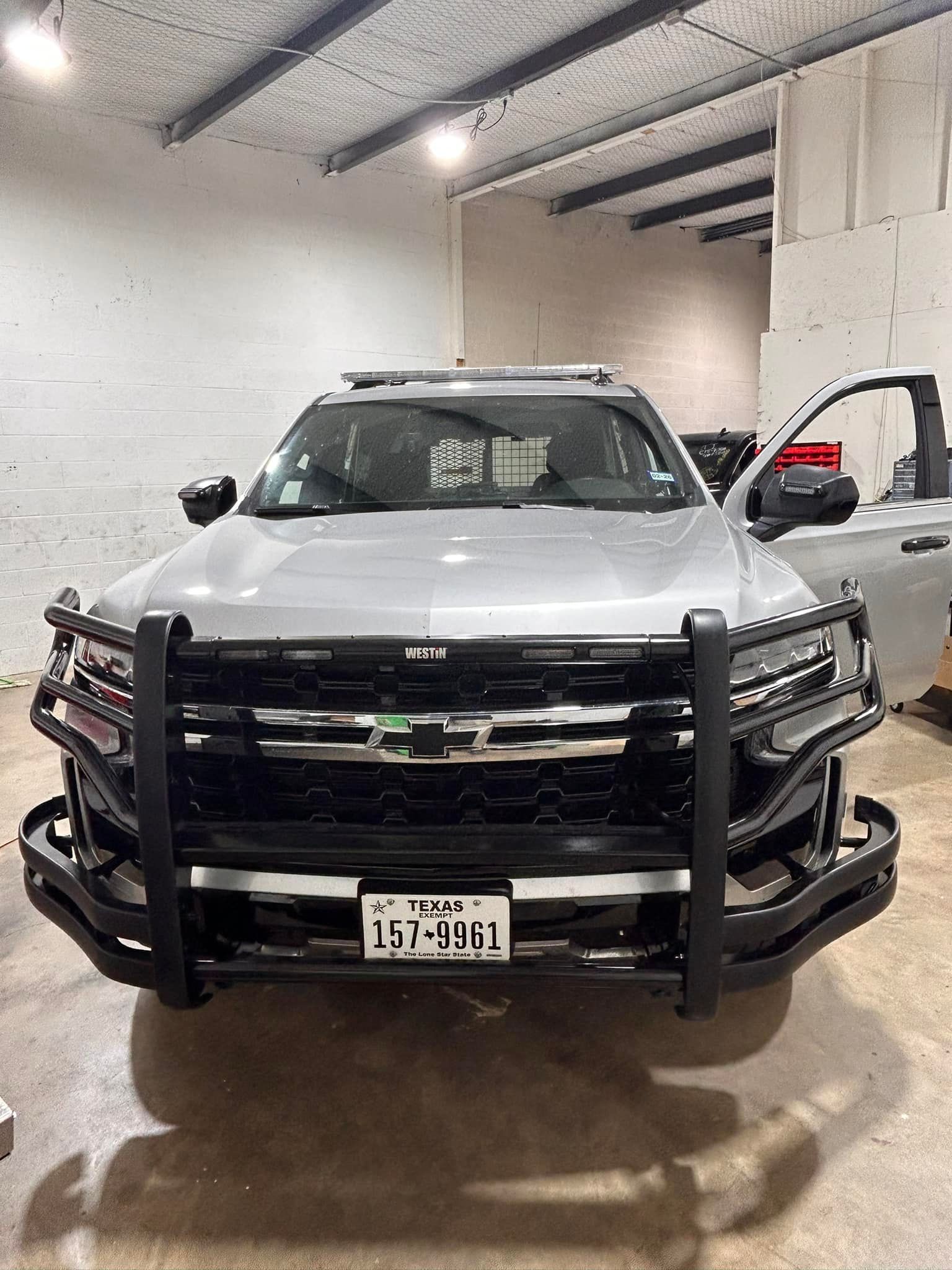 Silver police SUV with push bar, Texas license plate, door open, indoors.