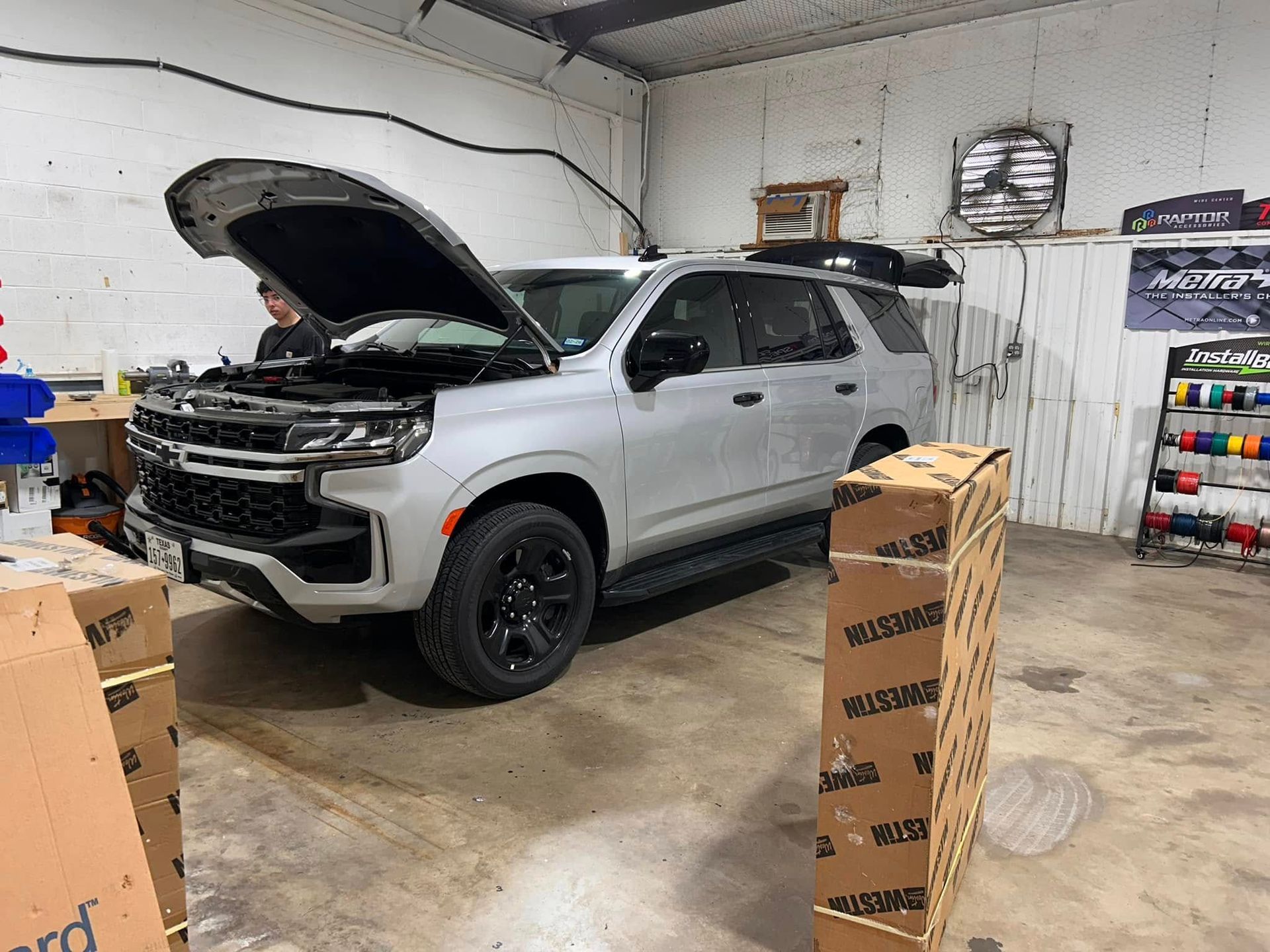 Silver SUV with open hood in a garage. Mechanic is working. Brown boxes in the foreground.