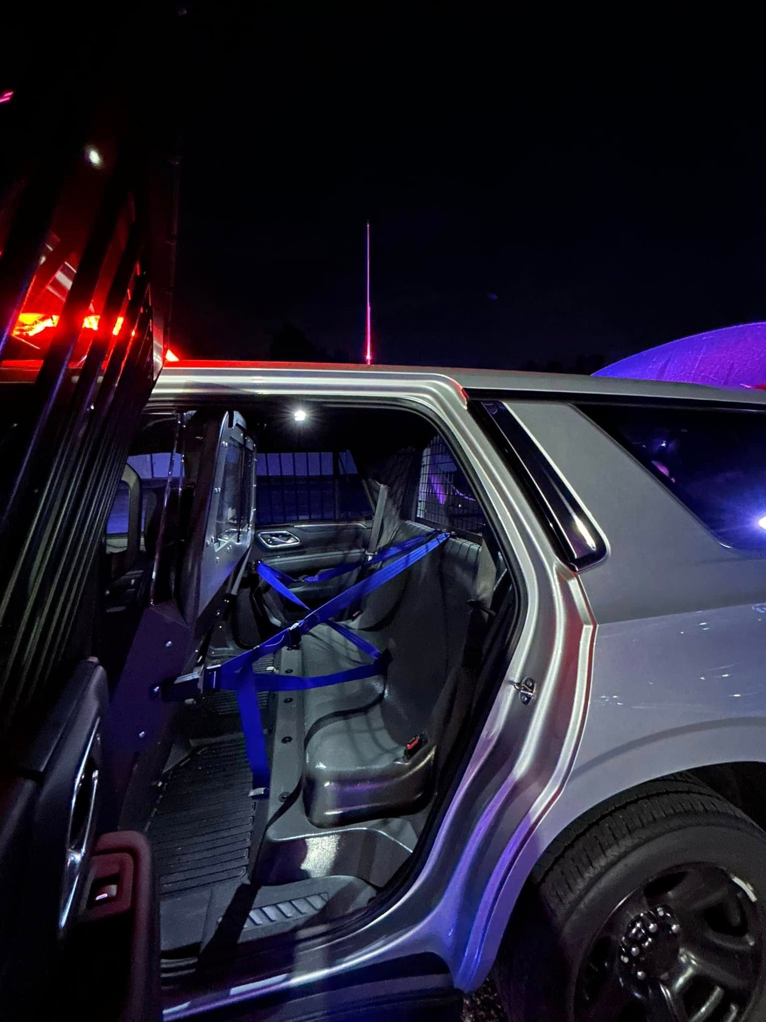 Open door of a gray truck revealing a seat with blue safety straps. Dark setting, likely at night.