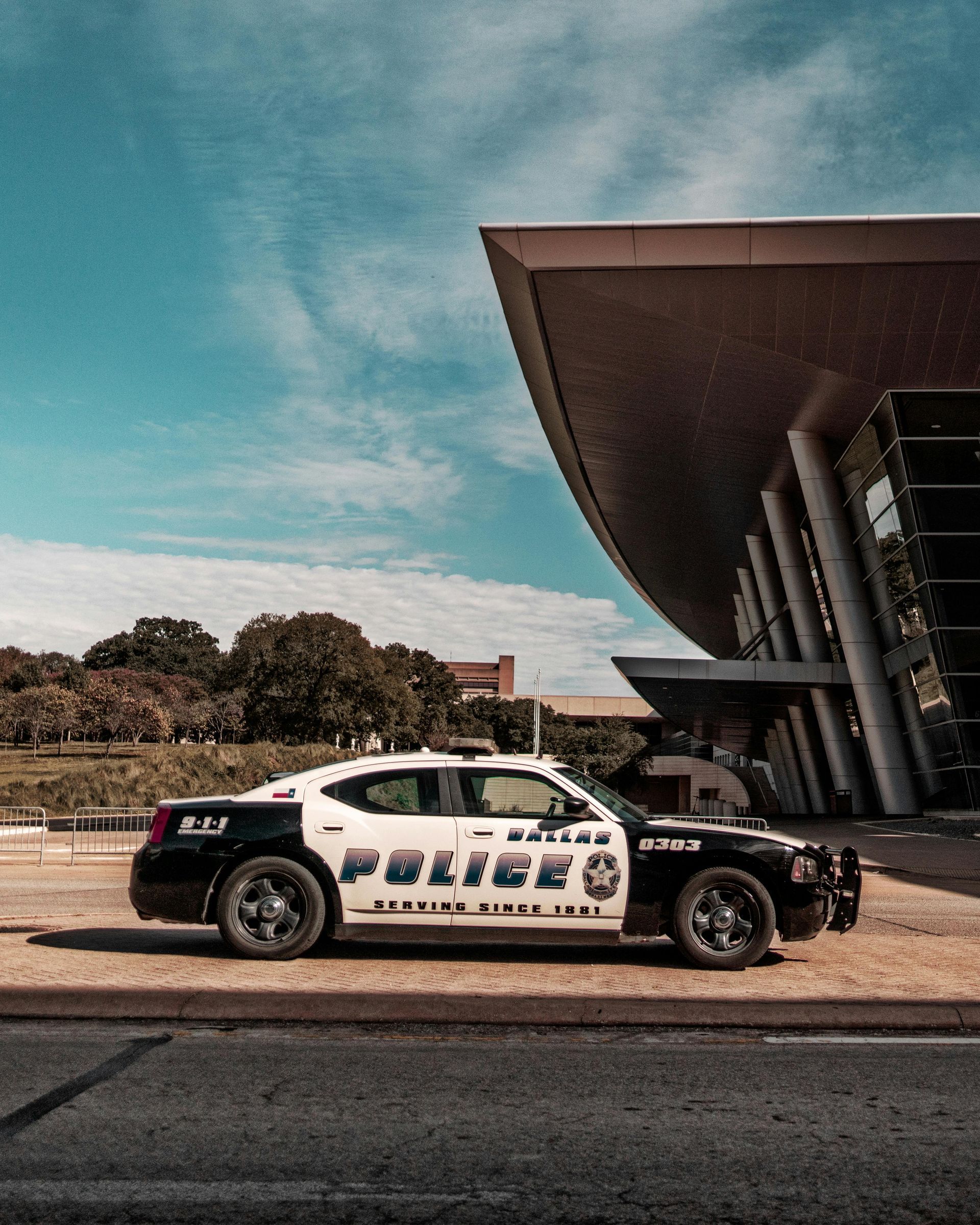 Police cruiser parked outside a modern building with a curved roof on a sunny day.