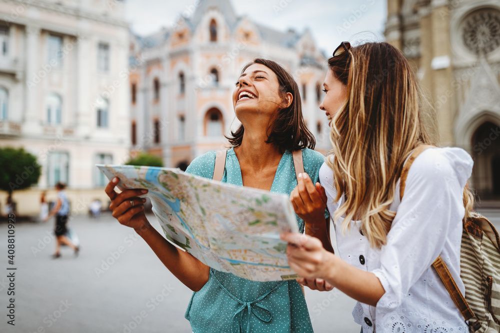 Two women laughing while looking at a map in a city square.