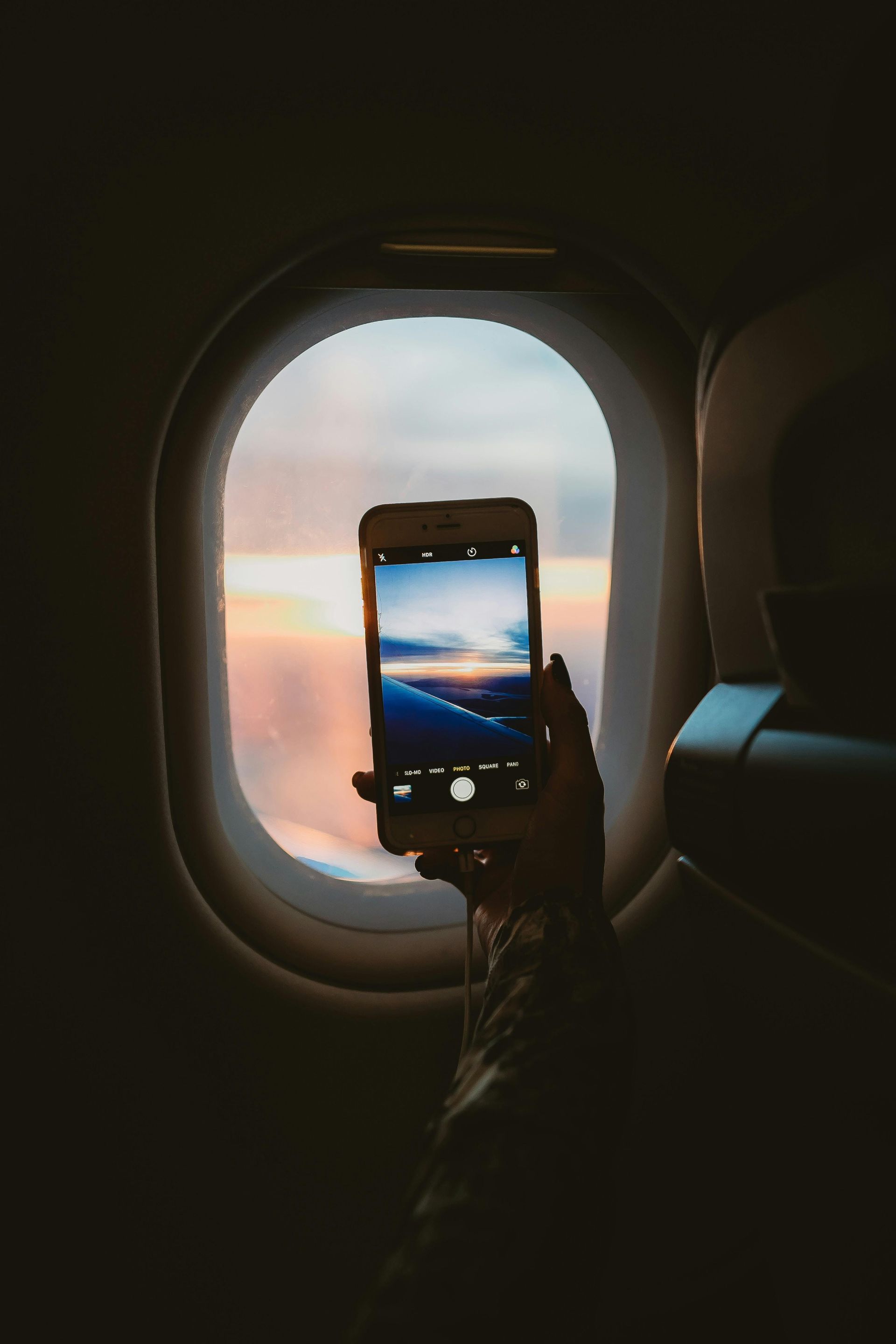 Person on a plane taking a photo of a sunset through the window with their phone.