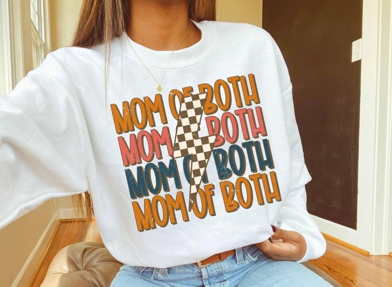 A woman wearing a white sweatshirt that says mom of both