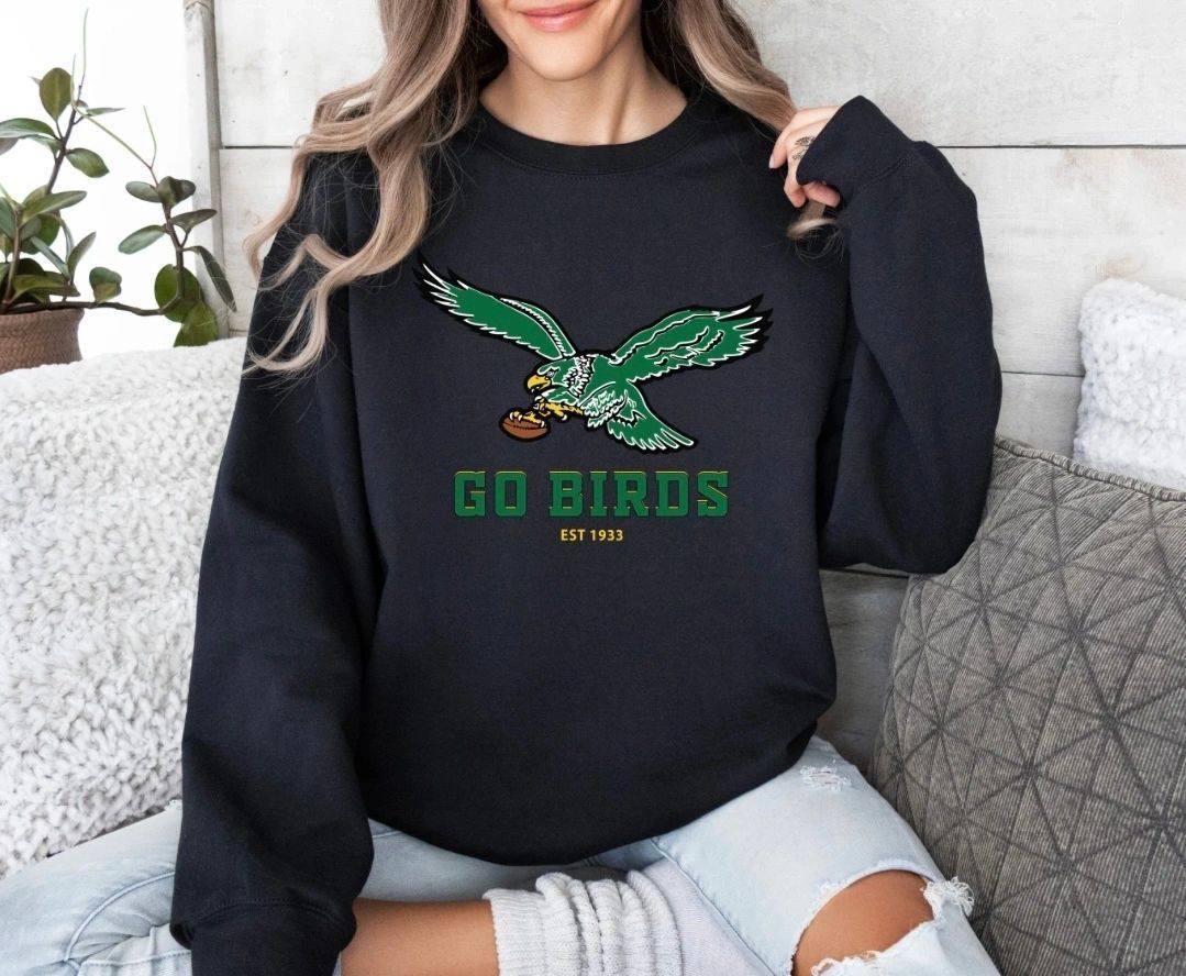 A woman is sitting on a couch wearing a go birds sweatshirt