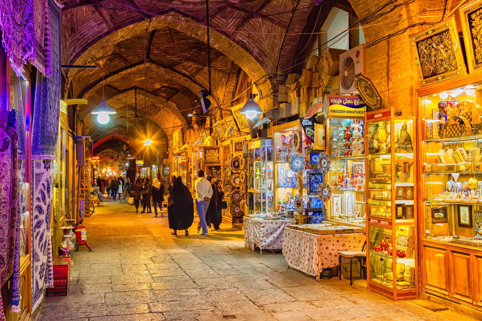 A group of people are walking down a narrow alleyway in a market at night.