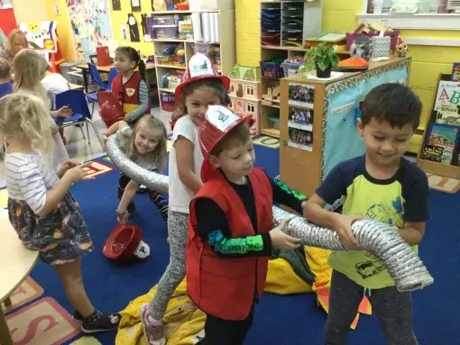 A group of children are playing with a fire hose in a classroom