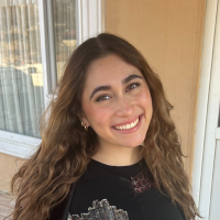 A woman with long hair is smiling for the camera while standing in front of a window.