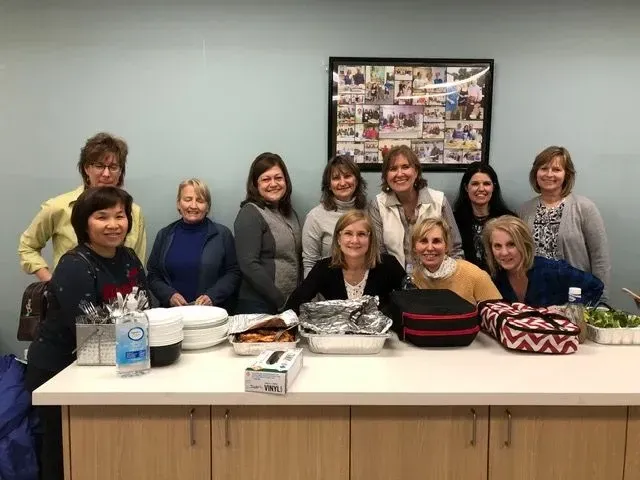 A group of women are posing for a picture in front of a counter filled with food.