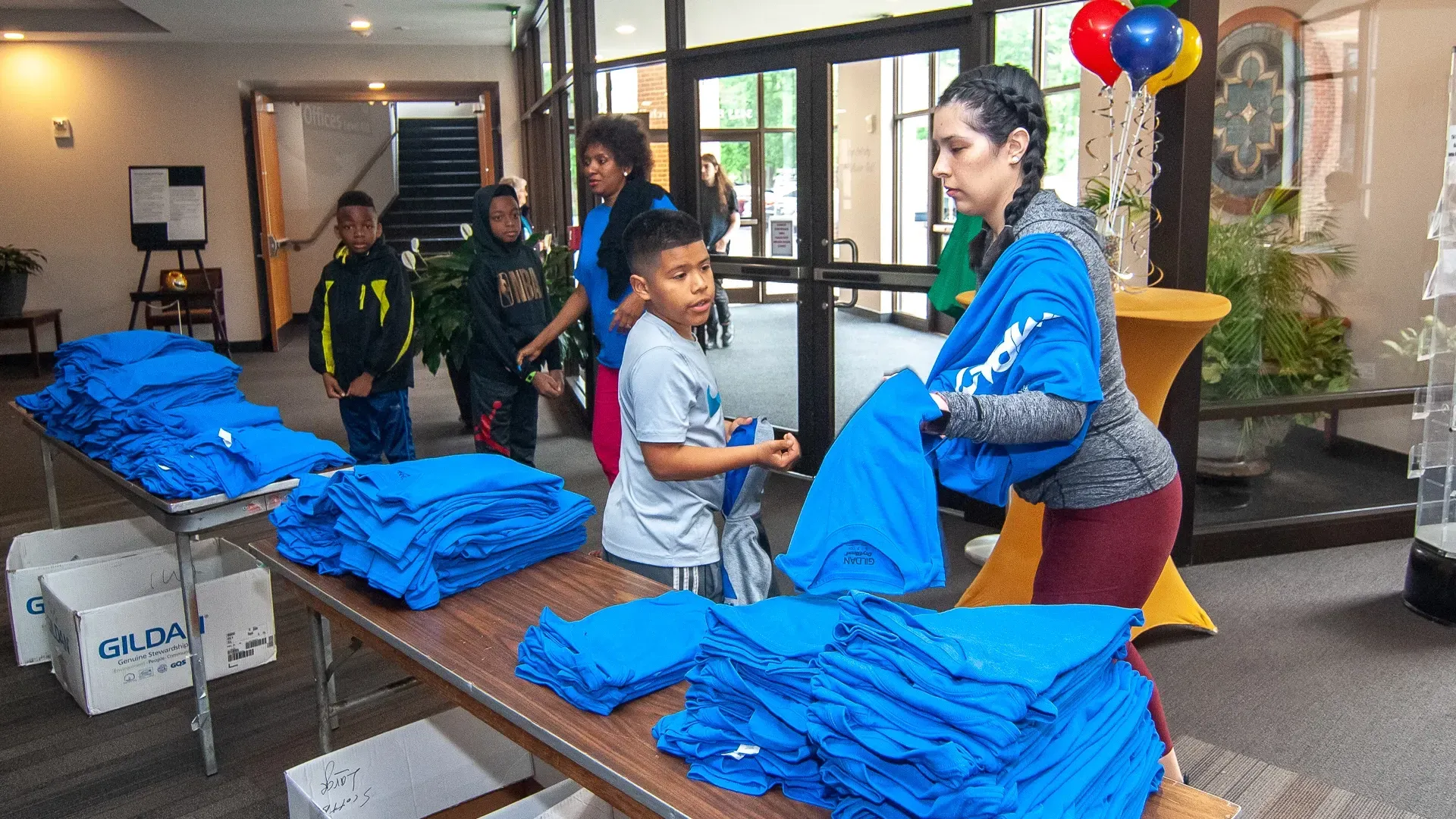 A woman is standing in front of a table filled with stacks of blue shirts.