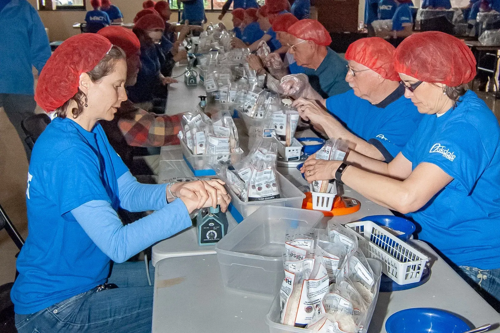 A group of people wearing blue shirts and red hats are working at a table