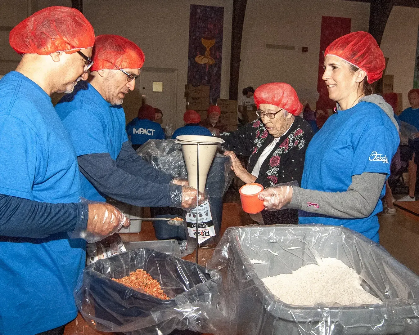 A group of people wearing blue shirts and red hair nets are preparing food