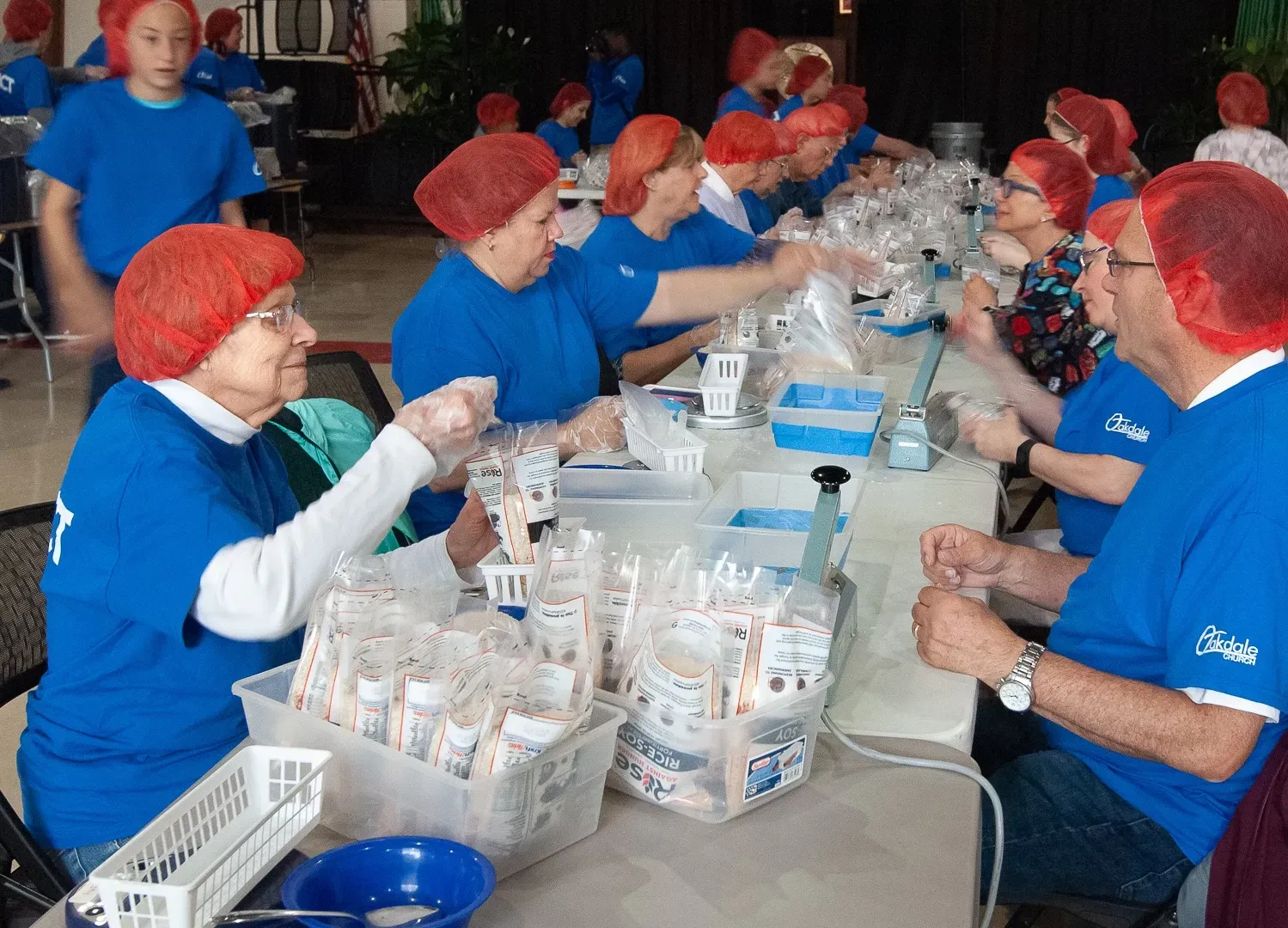 A group of people wearing blue shirts and red hats are working at a table