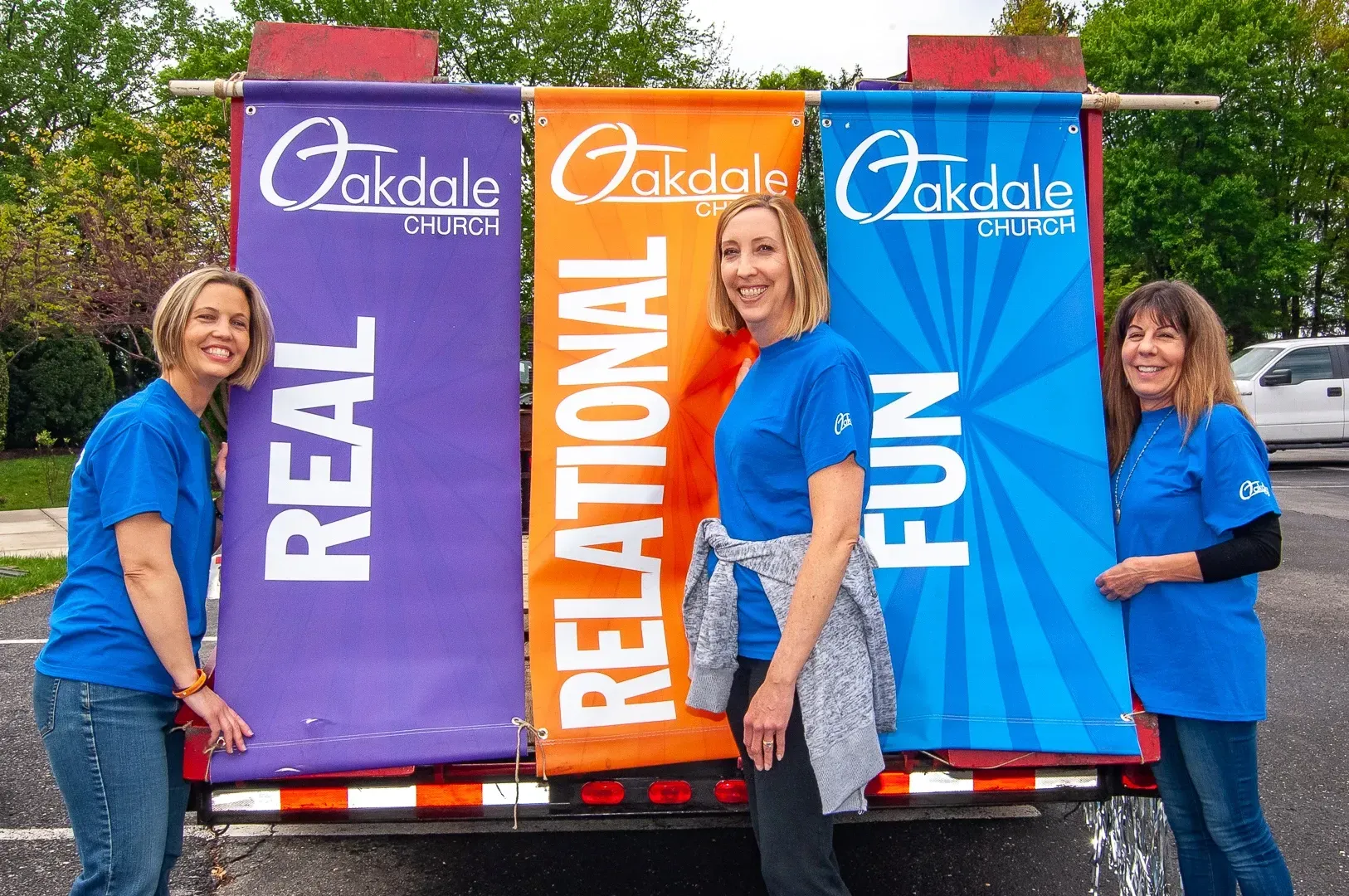 Three women are standing next to each other in front of a trailer with banners that say real relational fun.