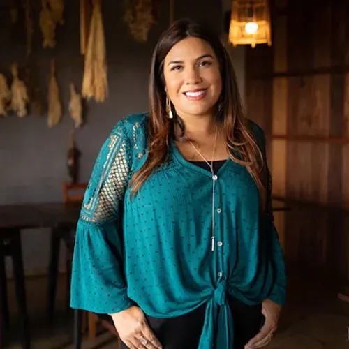 A woman is standing in a room wearing a green top and black pants.