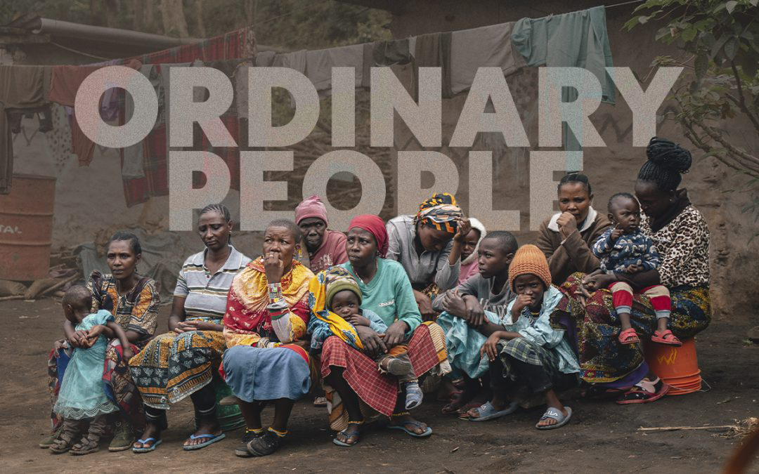 A group of people are sitting in front of a sign that says `` ordinary people ''.