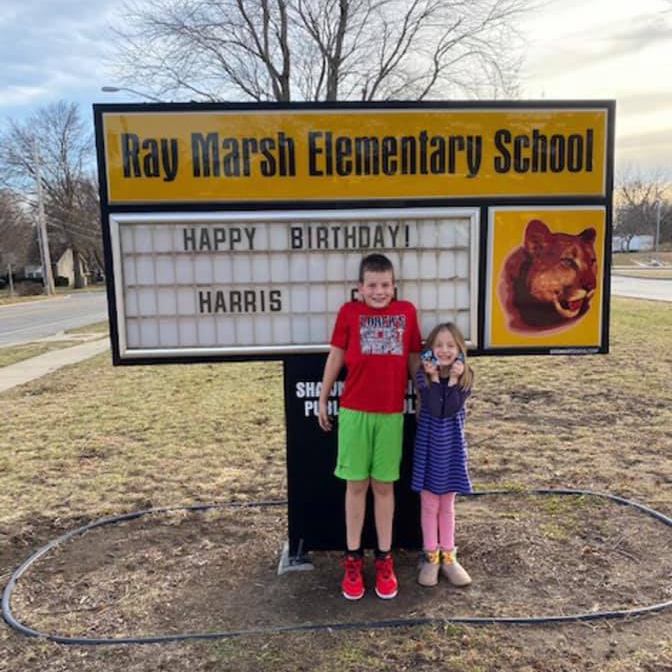 Two children standing in front of a ray marsh elementary school sign