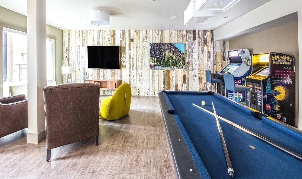 Recreation room with pool table, arcade games, TV, and seating against a wood-paneled wall.
