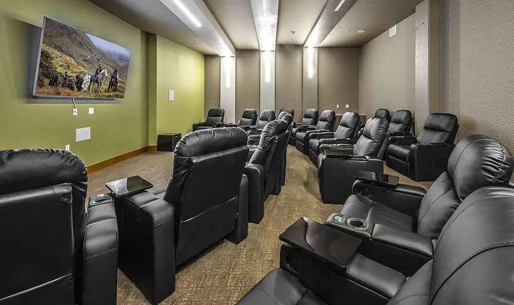 A small home theater with rows of black leather recliners facing a large TV screen.