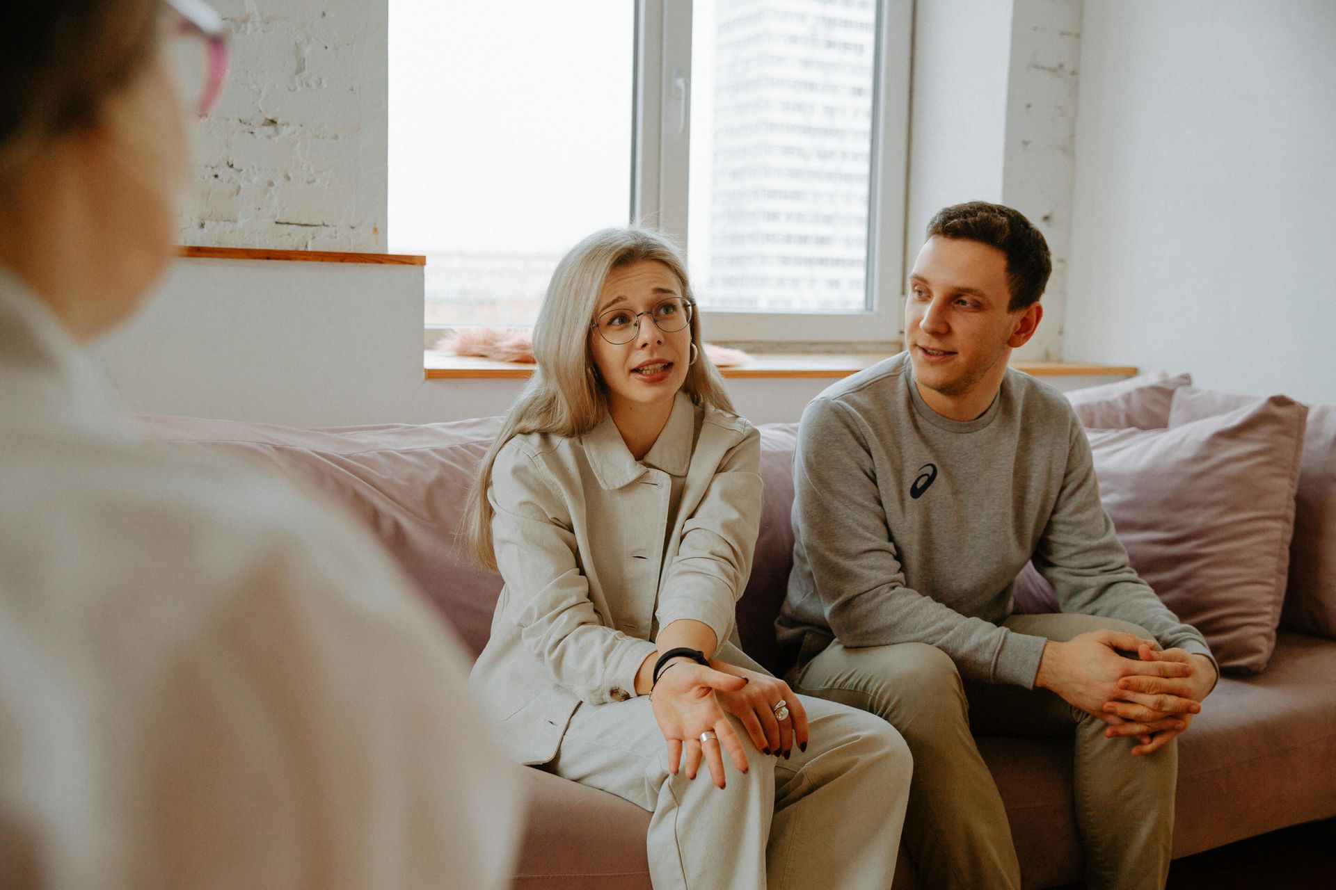 Couple in session with therapist on a couch in a room with a window.