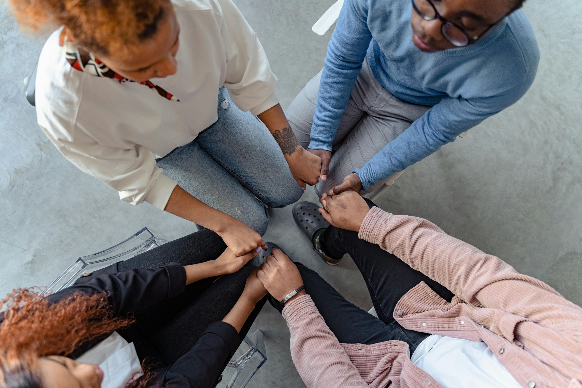 Four people sitting in a circle, holding hands.