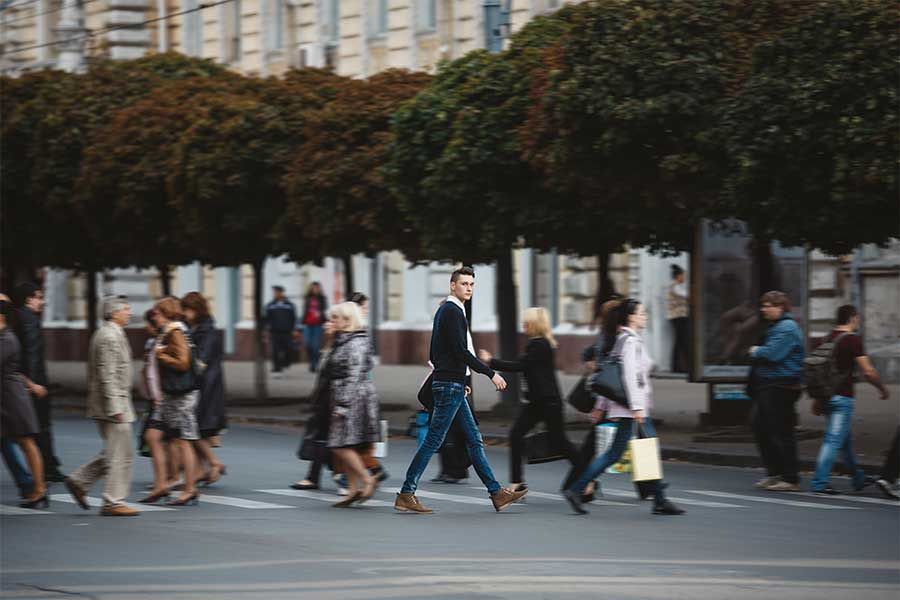 People crossing a street at a crosswalk in front of a row of trees; blurred background.