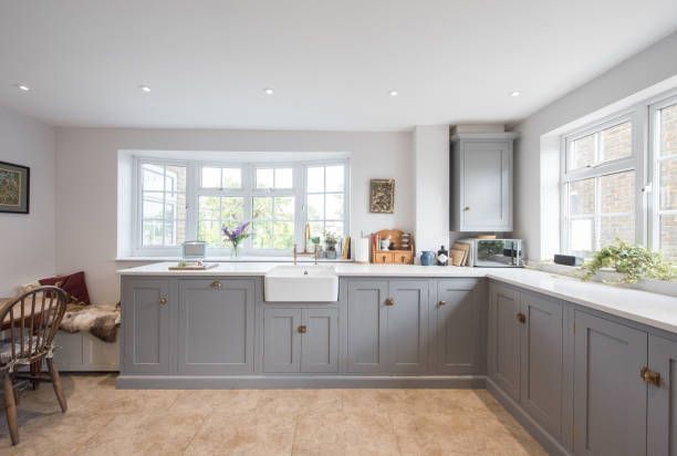 Gray kitchen with white countertops, sink, and windows. A built-in bench, cabinets, and a chair.