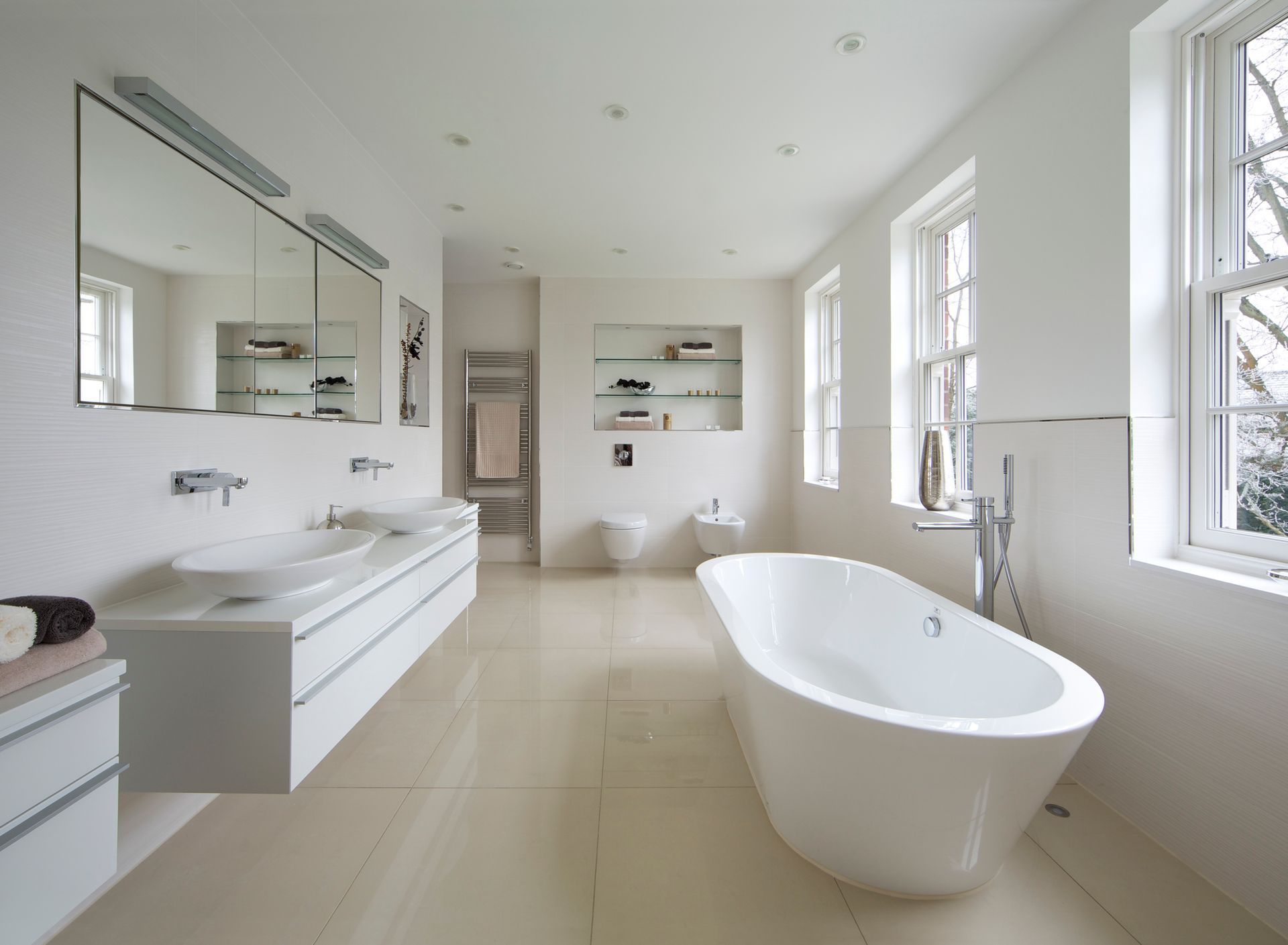 Bright white modern bathroom with a freestanding tub, double vanity, and large windows.