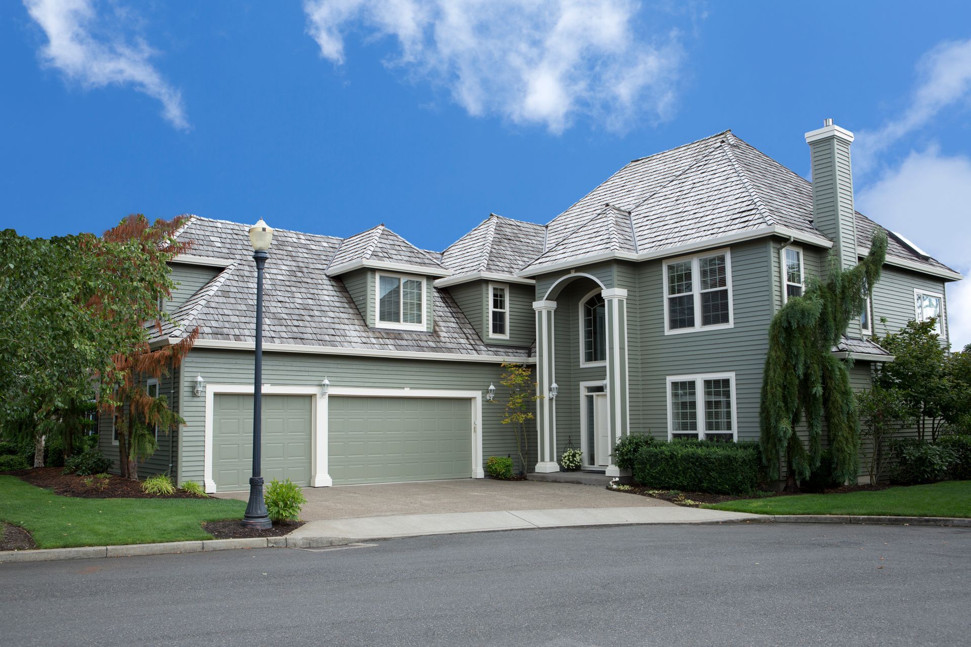 Two-story gray house with garage, arched doorway, and patterned gray roof under a blue sky.