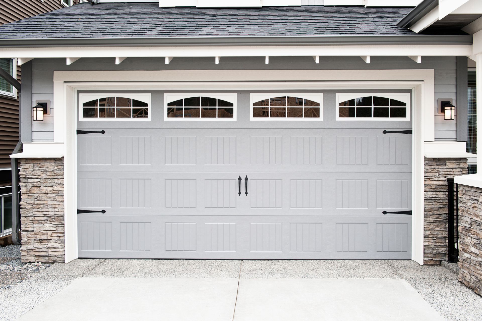 Gray garage door with decorative windows, black hardware, and stone accents.
