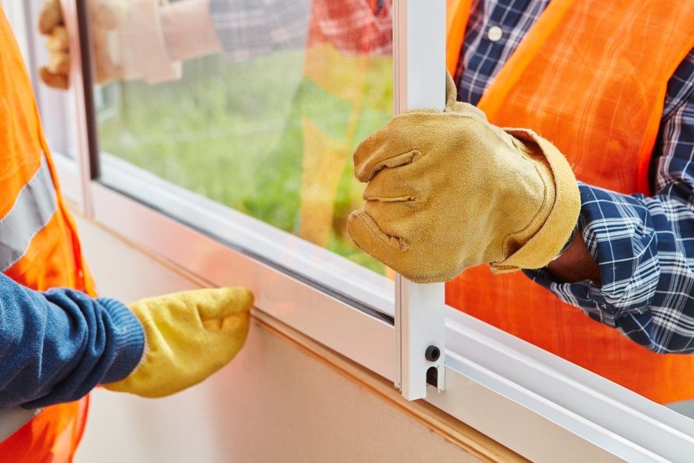 A Man Wearing Yellow Gloves Is Installing A Window — Northern Glazing Glass & Aluminium In Smithfield, QLD