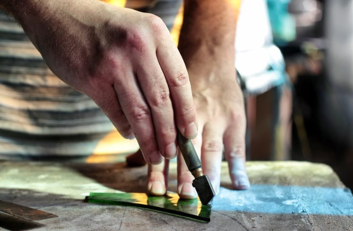 A Person Is Cutting A Piece Of Glass With A Glass Cutter — Northern Glazing Glass & Aluminium In Torres Strait Islands, QLD