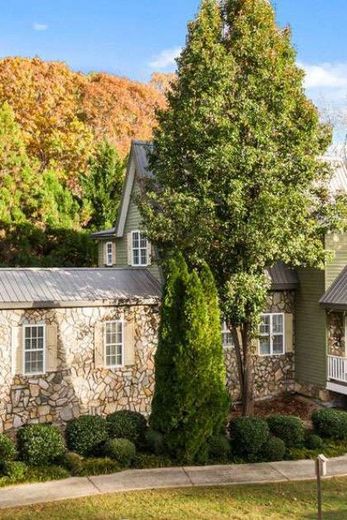 Stone and green-sided building with multiple windows, surrounded by trees with fall foliage and evergreens.