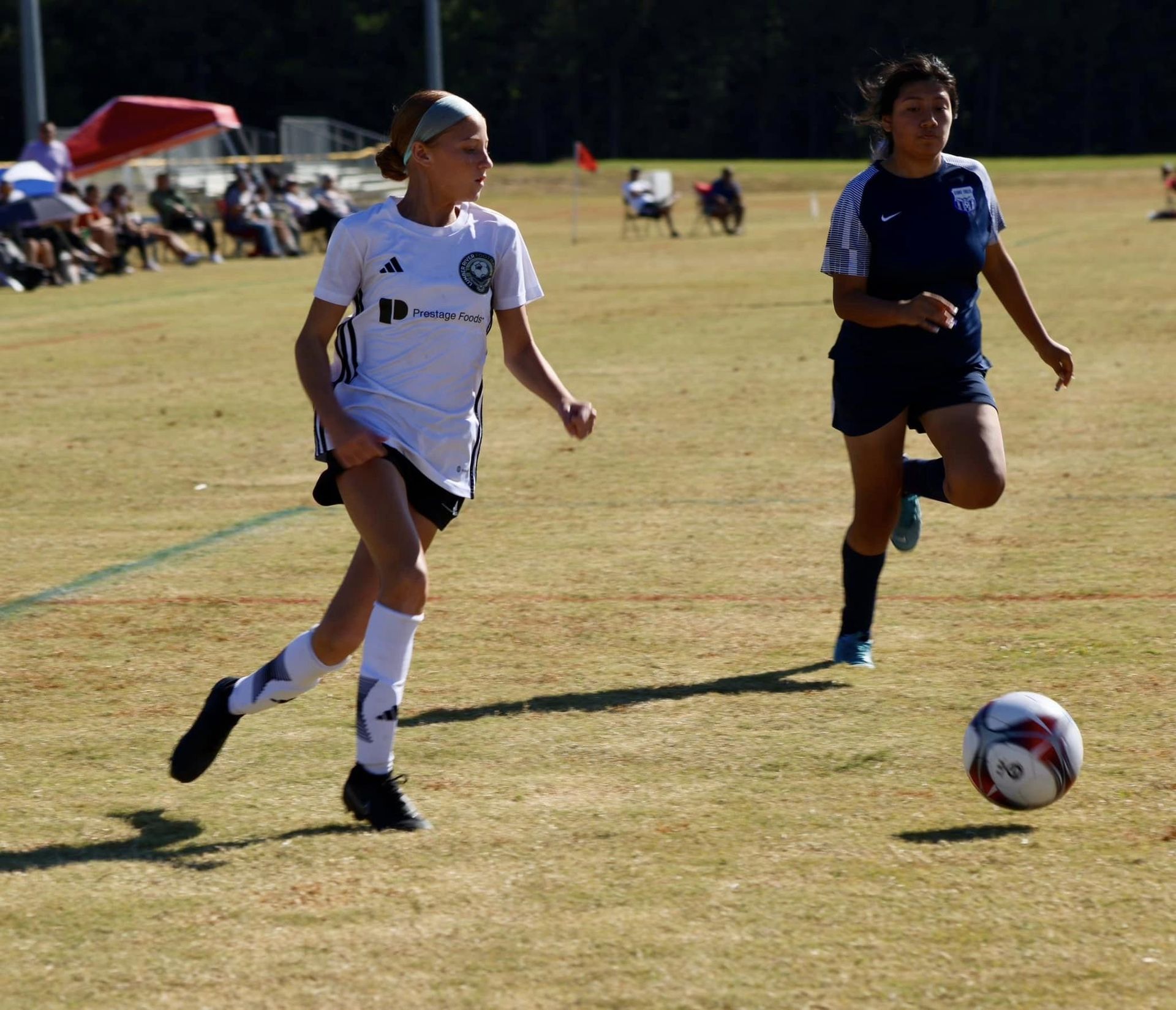 Two girls are playing soccer and one has the number 18 on her jersey