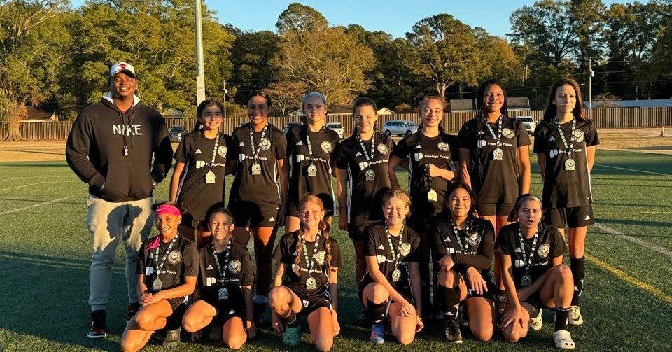 A group of young girls are posing for a picture on a soccer field.