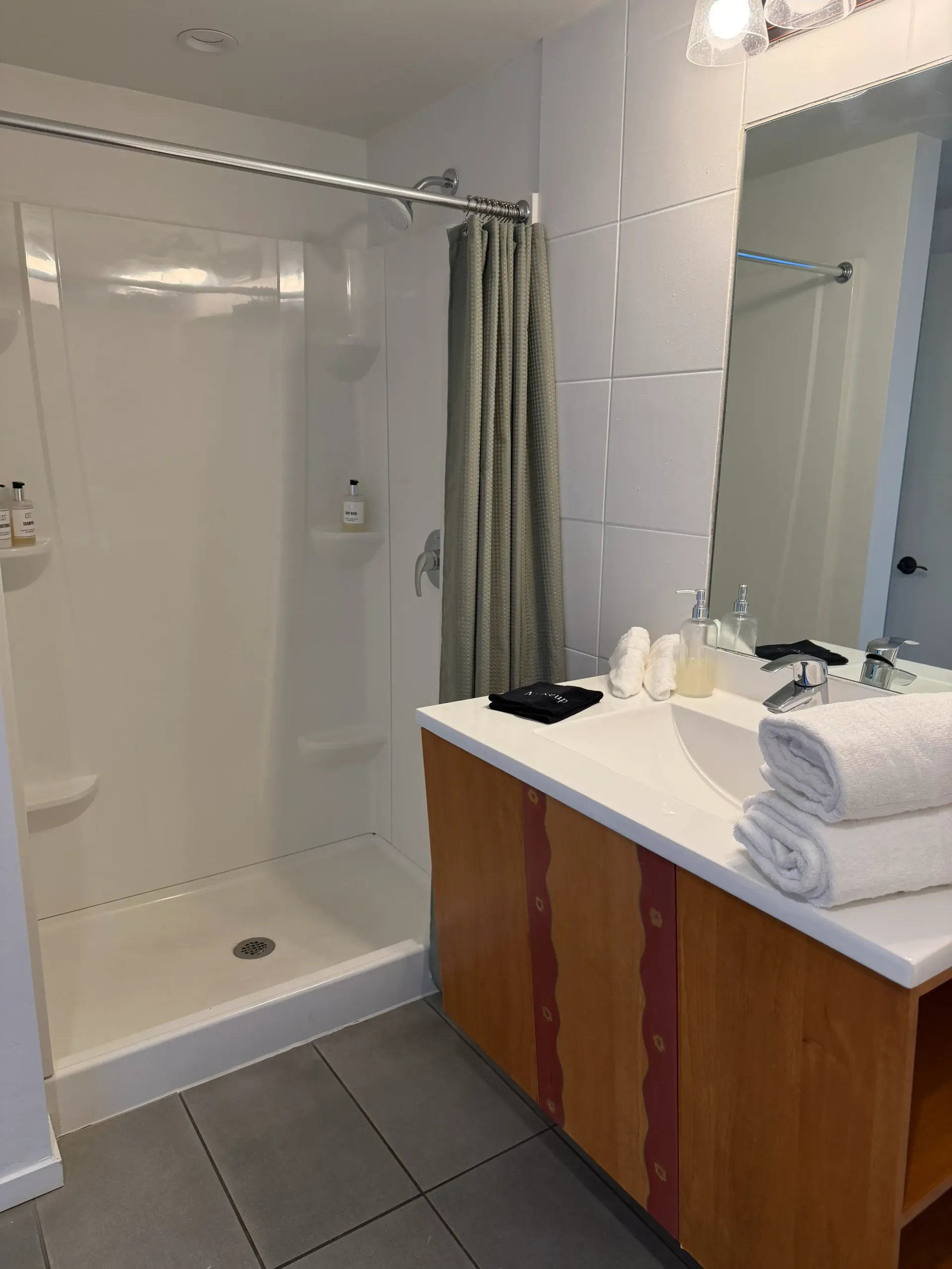 A bathroom featuring a shower stall with a grey curtain, a wood-cabinet vanity with a white sink, and folded white towels.
