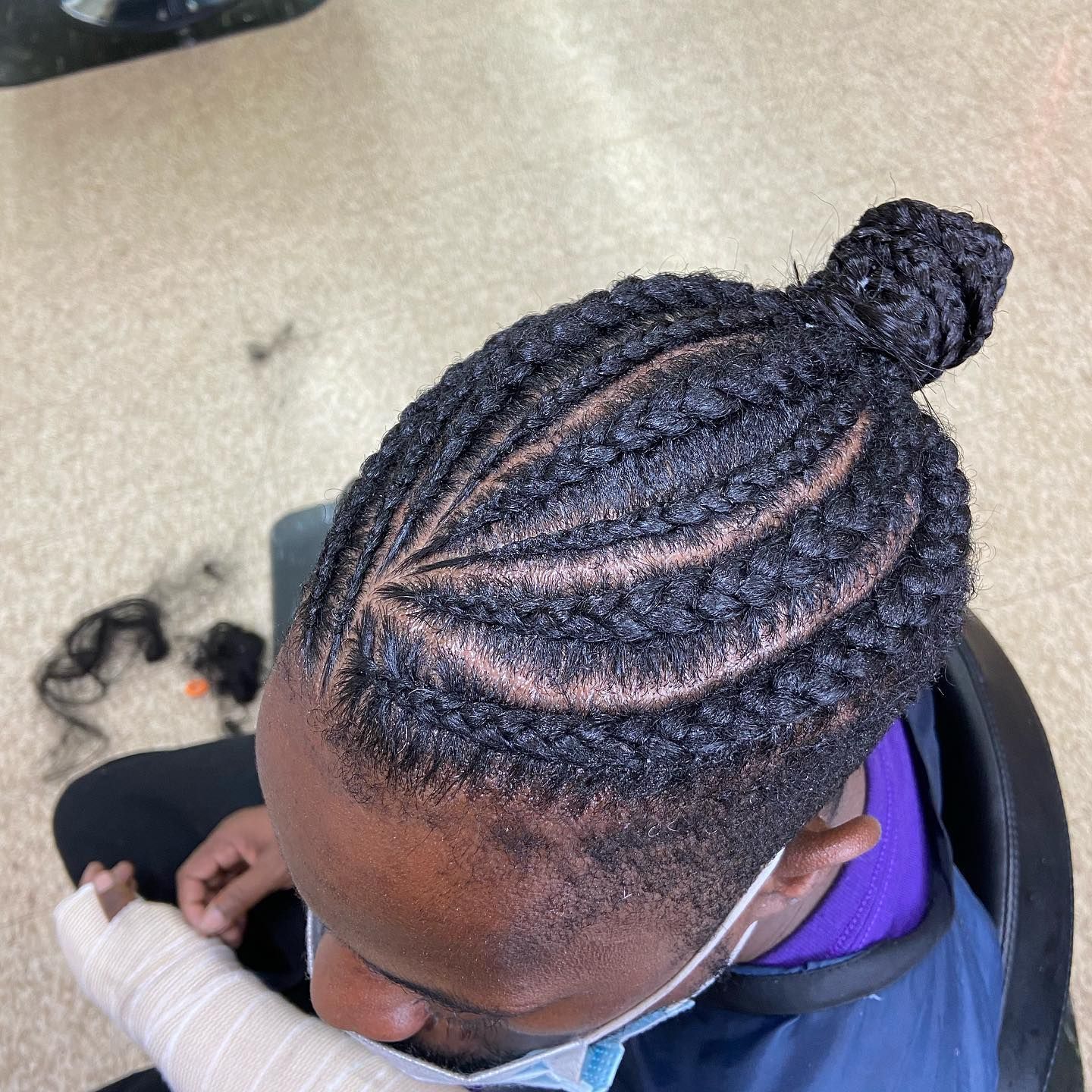 Man with cornrowed hair in a bun. Diagonal part, close-up shot, wearing a face mask.