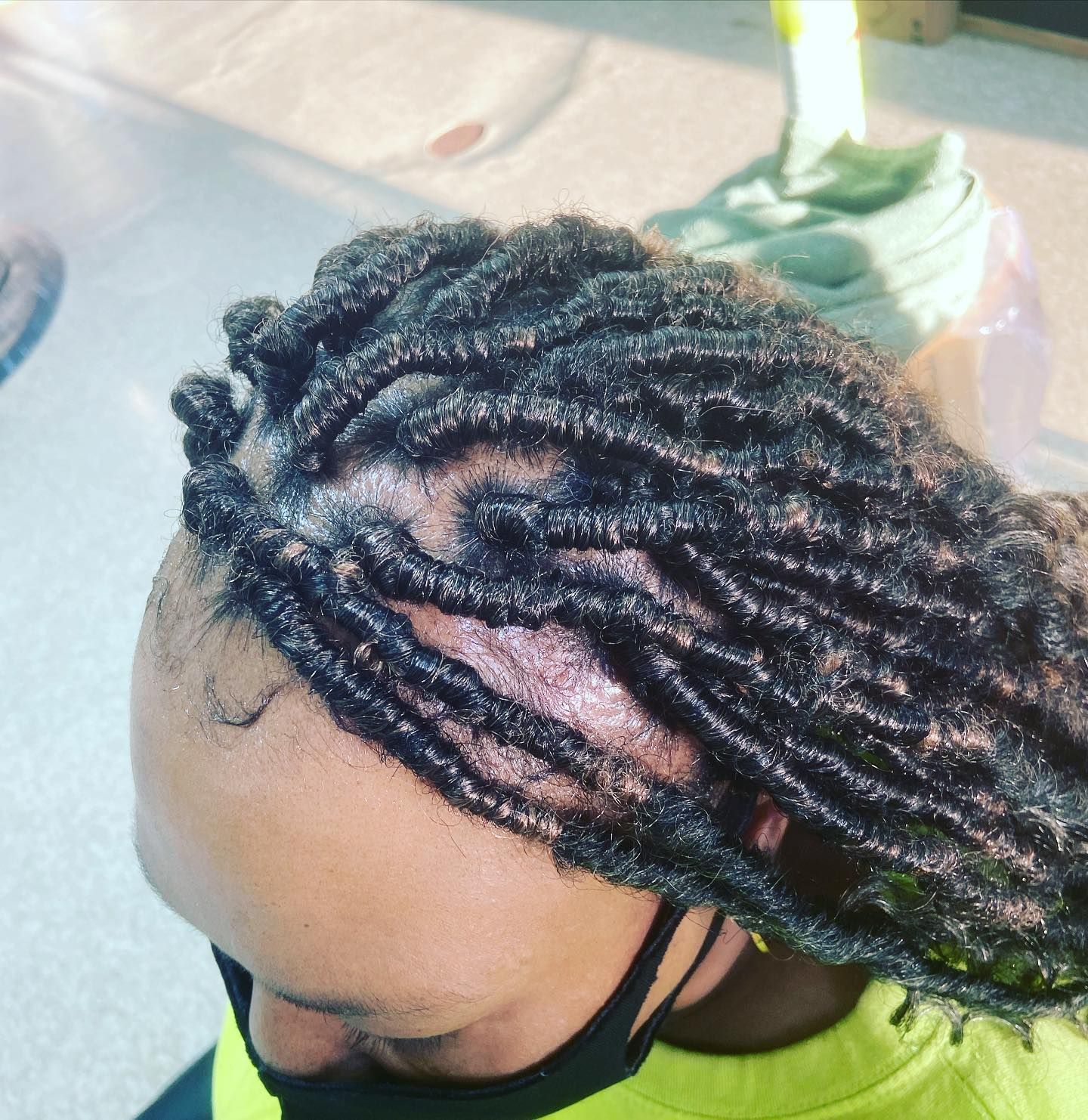 Close-up of a person's head with small, dark-colored locs. They wear a black face mask.
