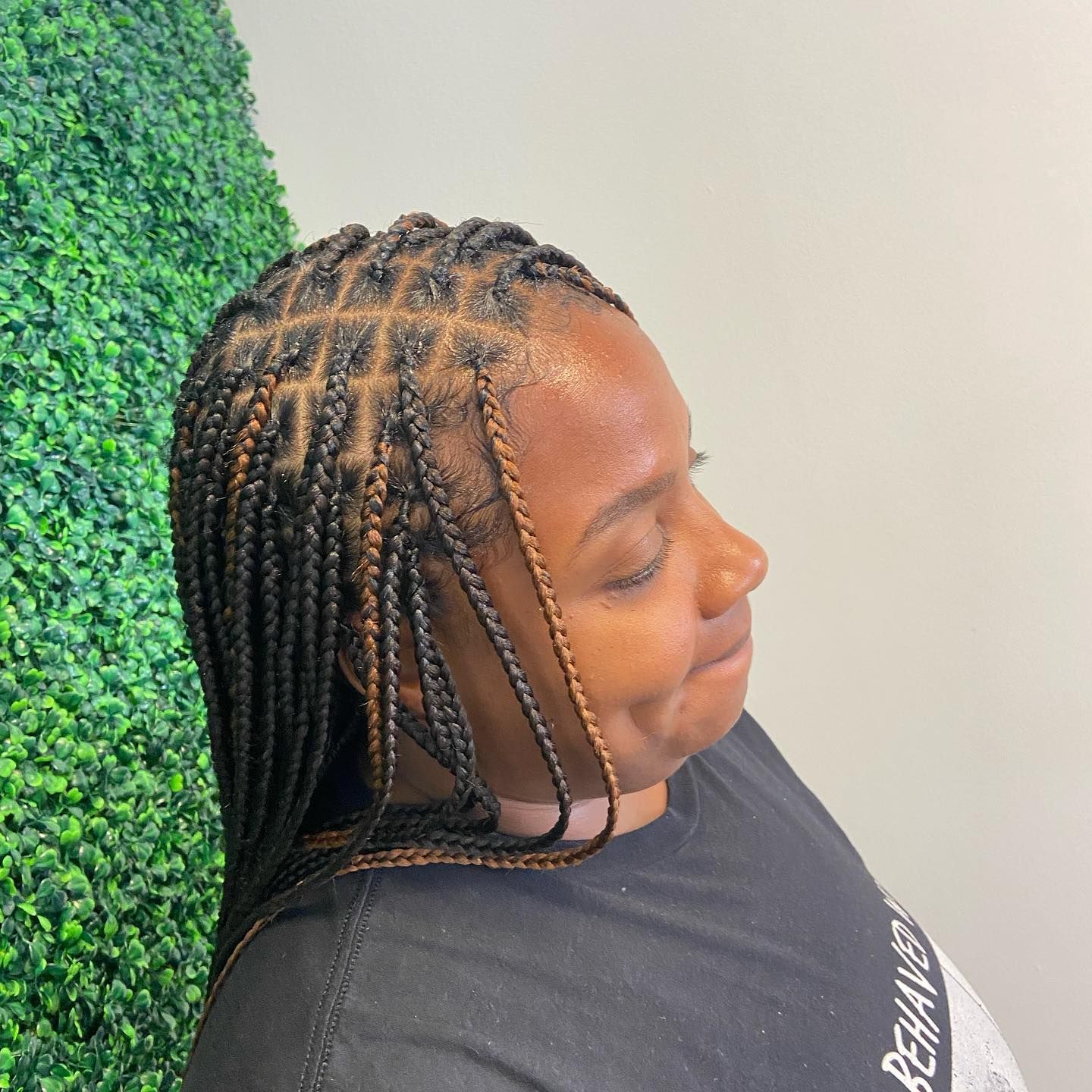 Woman with box braids smiles, in front of a green wall, wearing a black shirt.