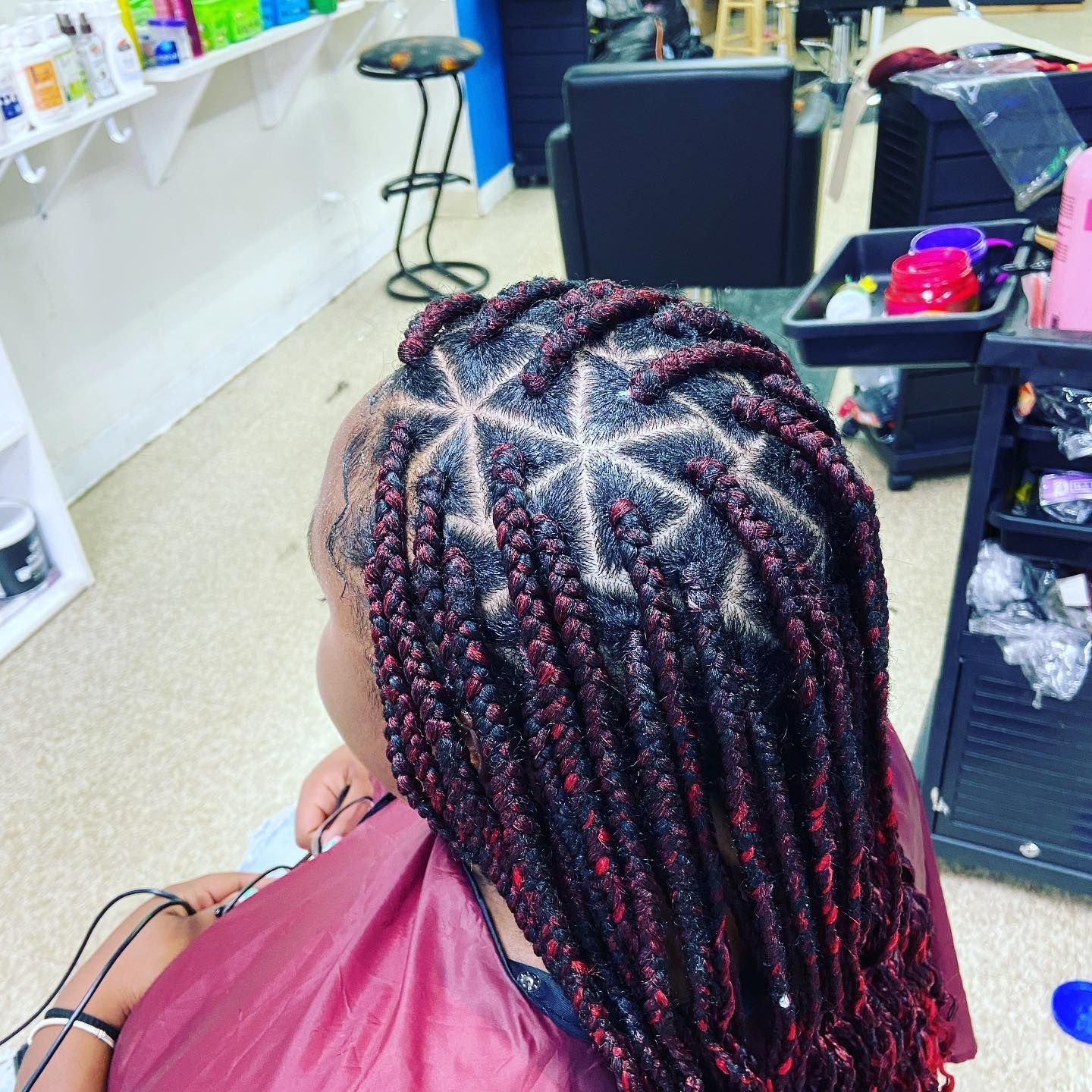 Braided hairstyle with red highlights, overhead view. Braids arranged in a geometric star design on the crown.