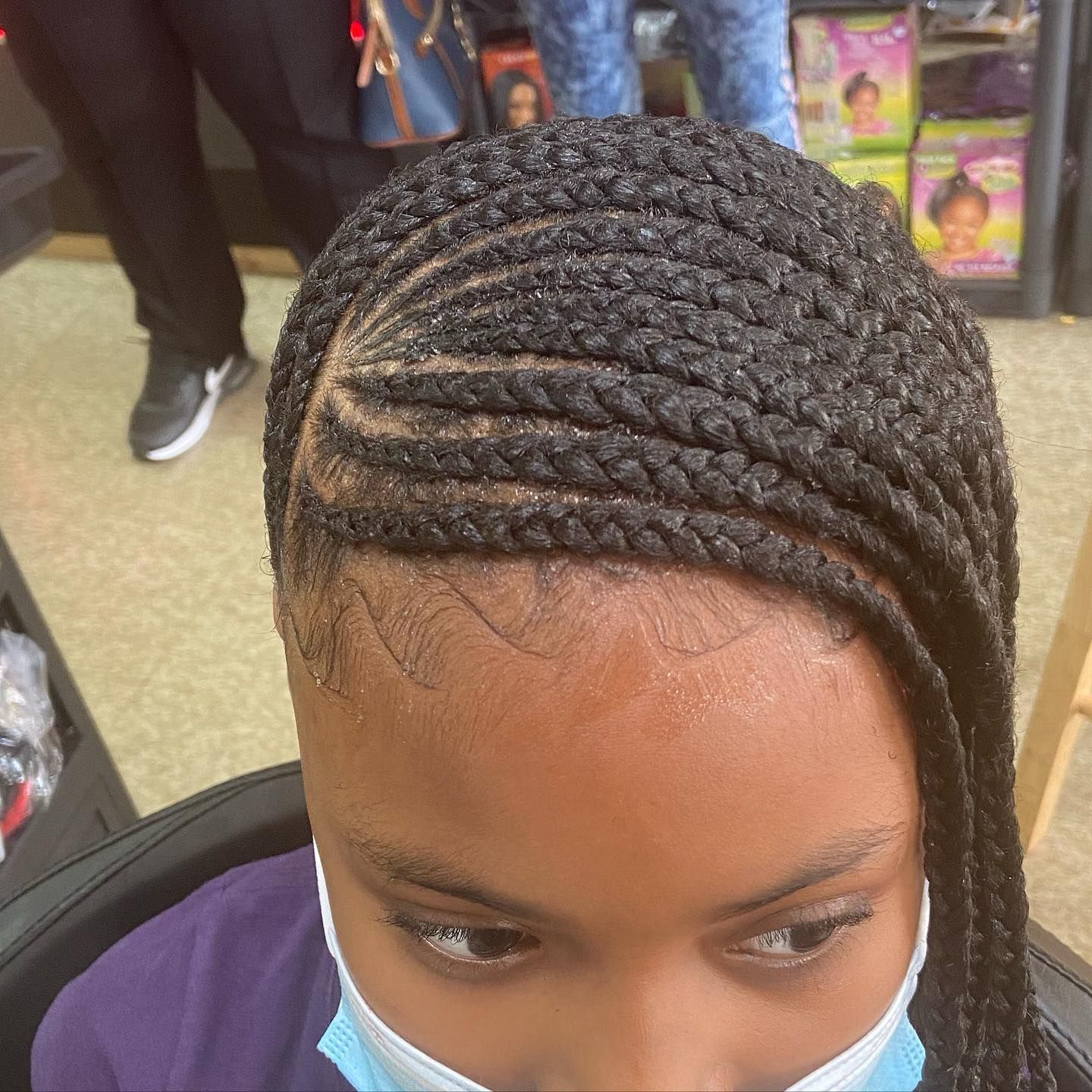 Close-up of cornrow braids styled on a person's head, wearing a face mask in a hair salon.