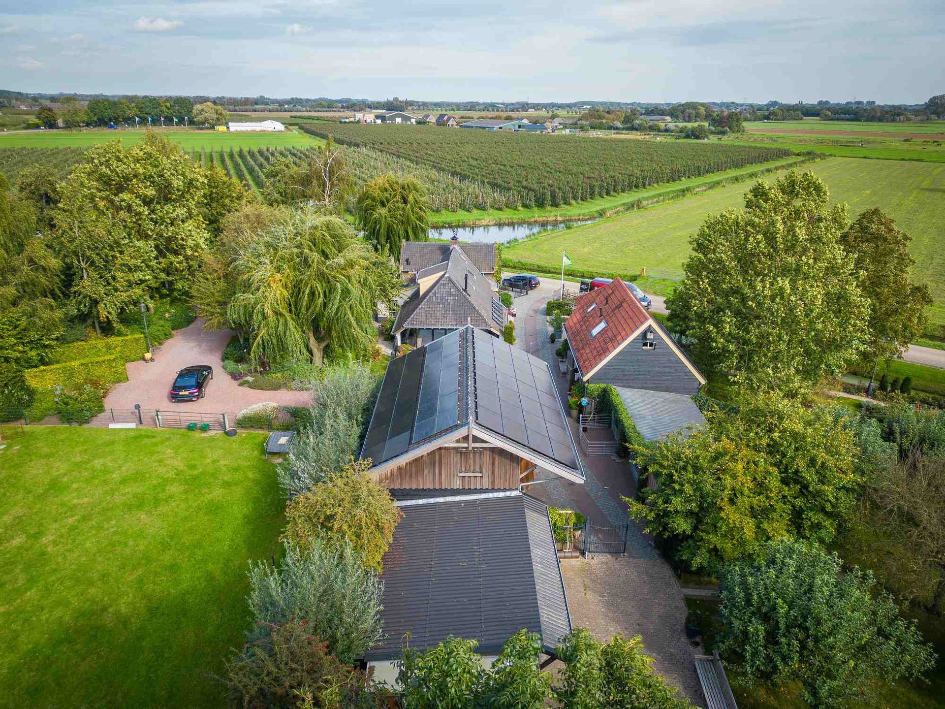 Een luchtfoto van een huis midden in een veld, omgeven door bomen.