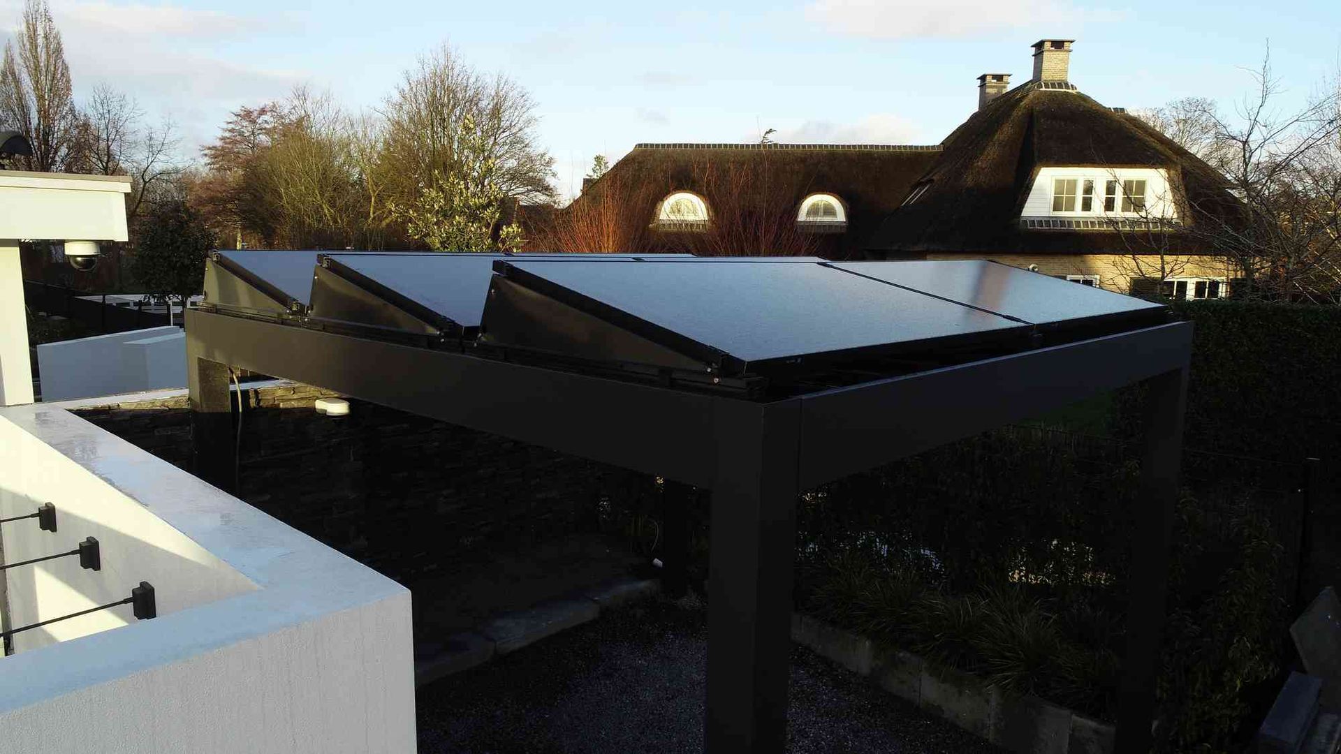 Een carport met zonnepanelen op het dak en een huis op de achtergrond
