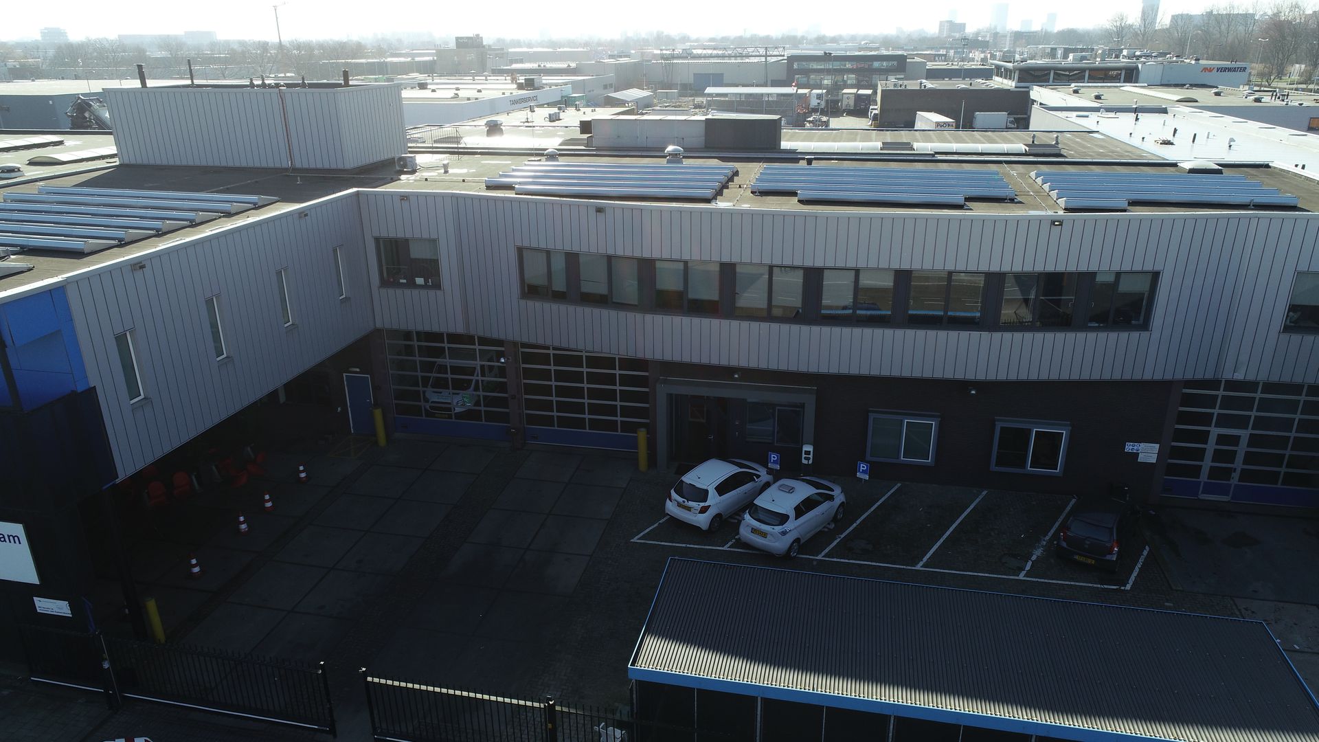 Een luchtfoto van een groot gebouw met daarvoor geparkeerde auto's.