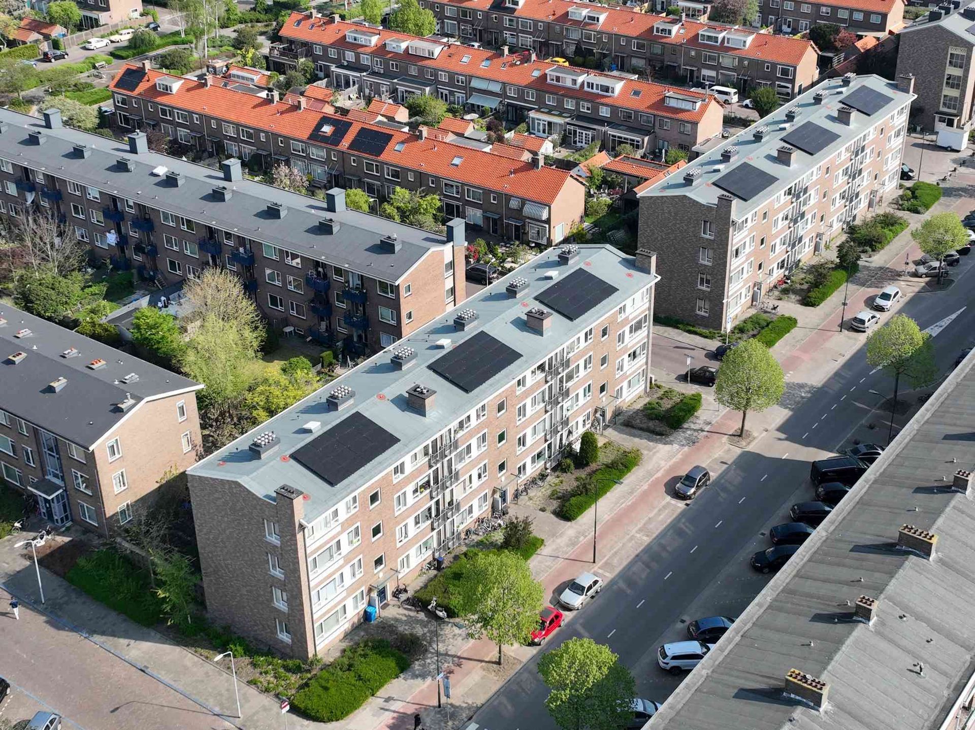 Een luchtfoto van een woonwijk met veel gebouwen en zonnepanelen op de daken.