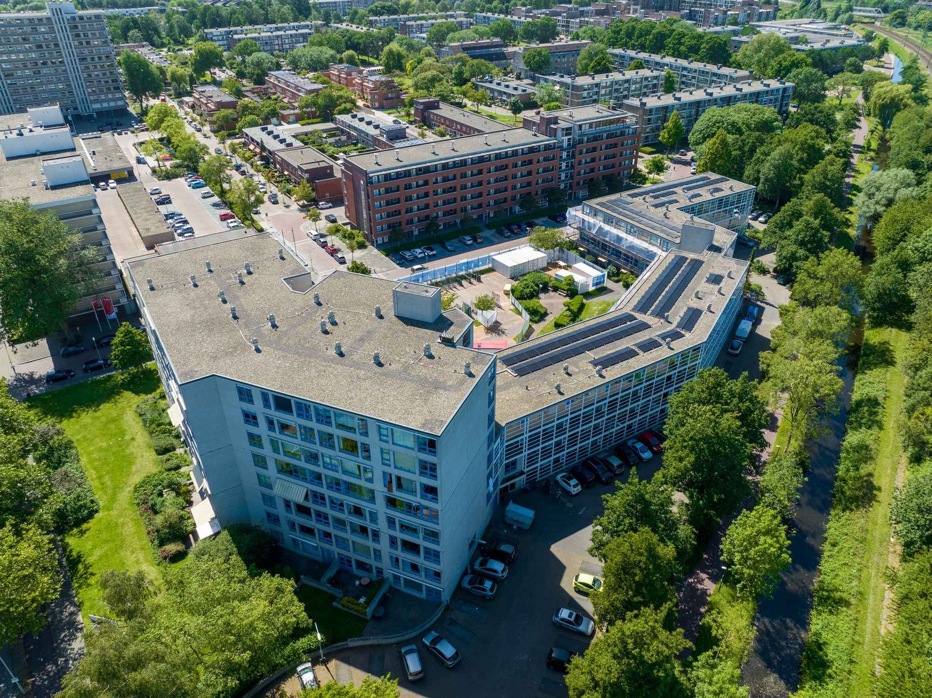 Een luchtfoto van een groot gebouw met zonnepanelen op het dak, omgeven door bomen.