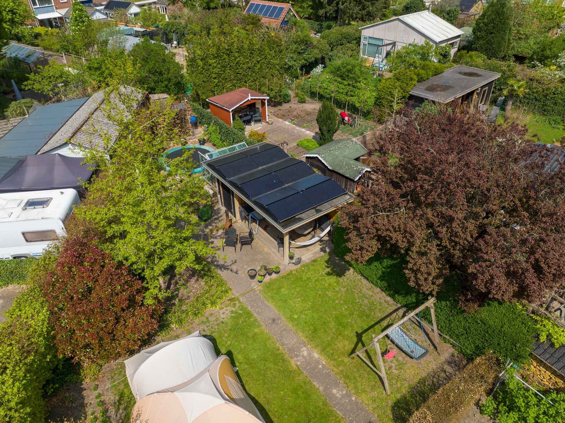 Een luchtfoto van een huis met zonnepanelen op het dak, omgeven door bomen.